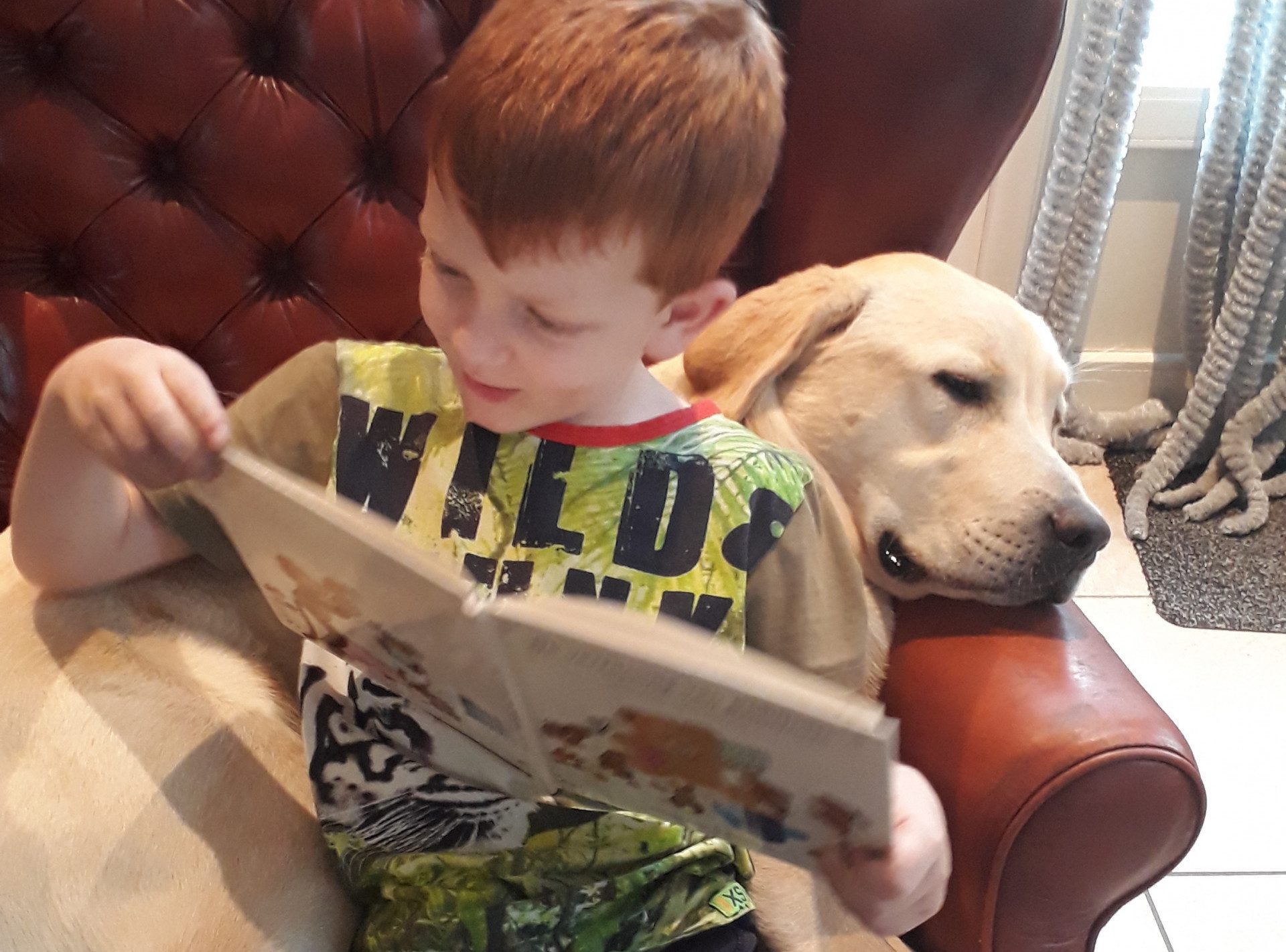 Ferry zit in een stoel en leest een boekje, Labrador Guus ligt achter hem te slapen