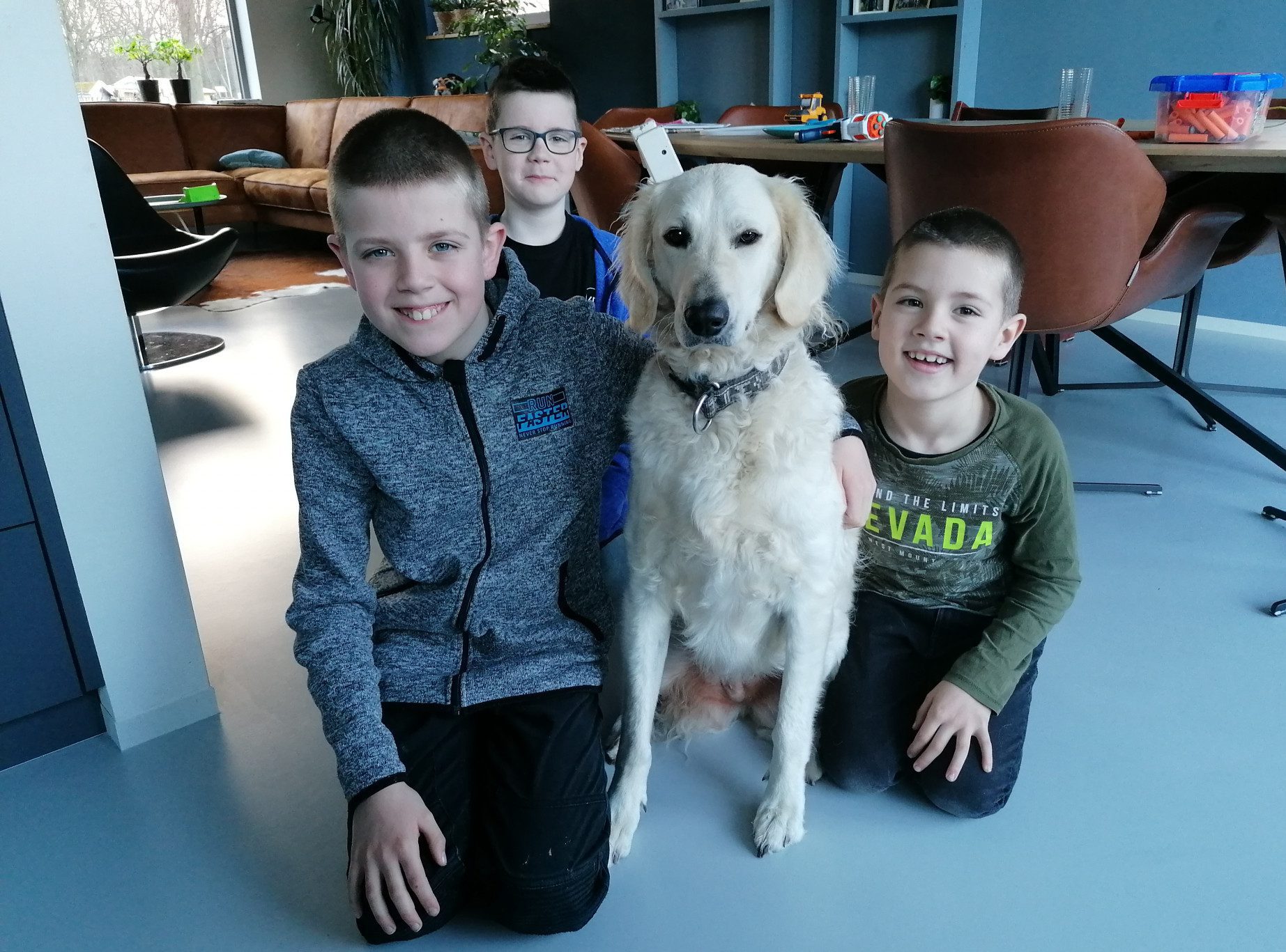 De drie kinderen uit het gezin zitten blij naast hun blonde labradoodle Bobbie