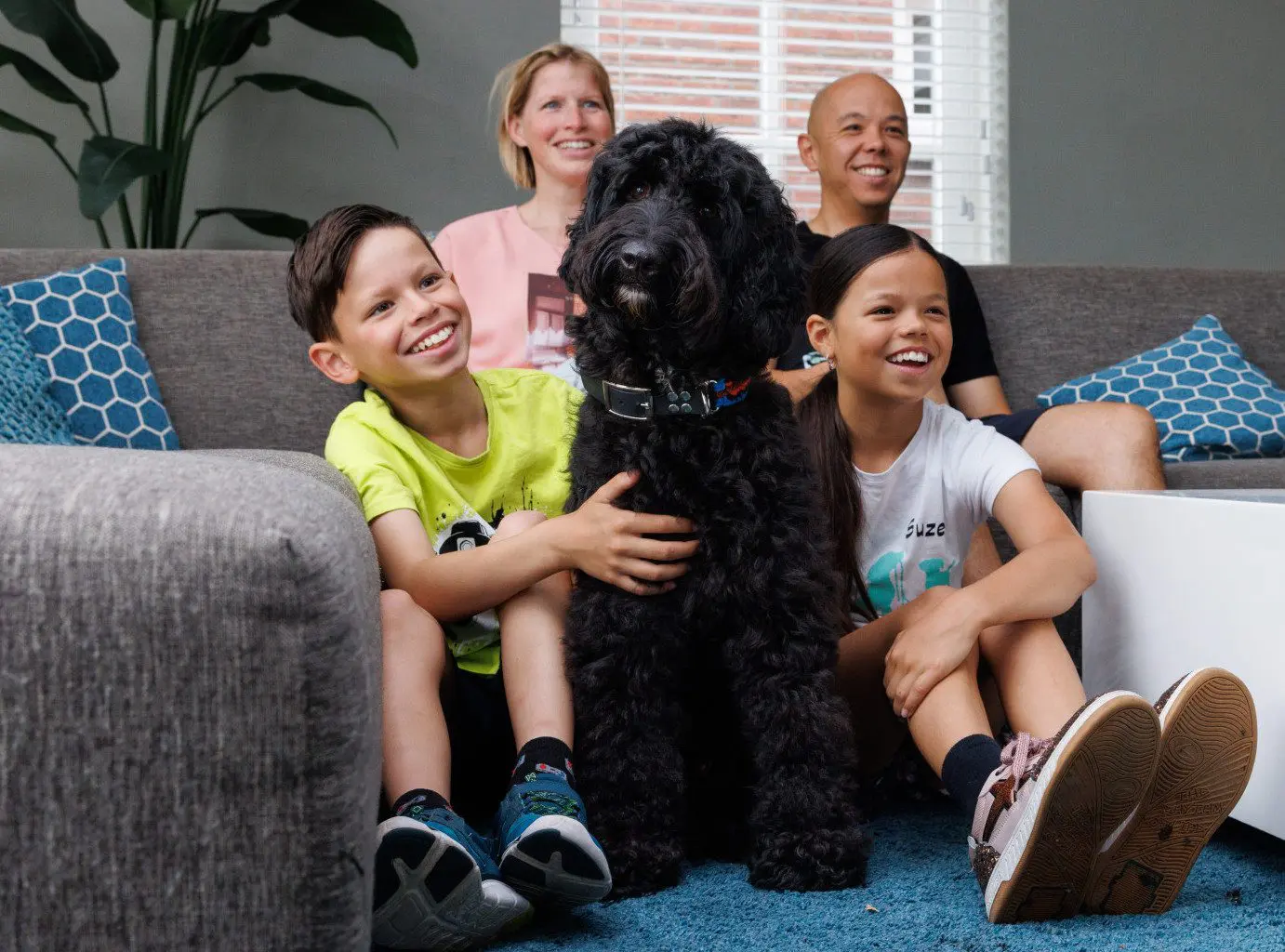 Het gezin Mei zit gezamenlijk op de bank terwijl hond Spot in het midden zit van de kinderen
