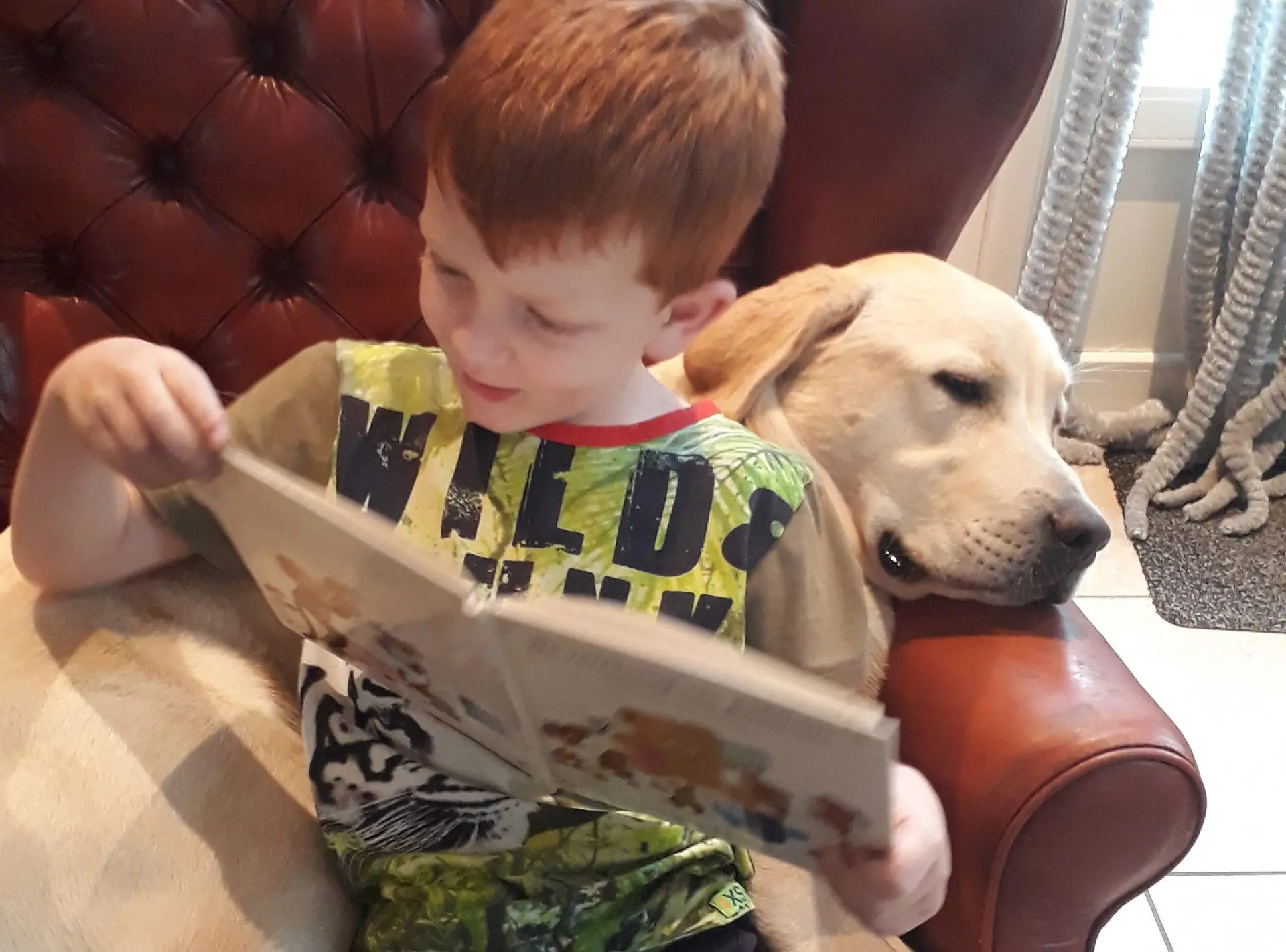 Ferry zit in een stoel en leest een boekje, Labrador Guus ligt achter hem te slapen