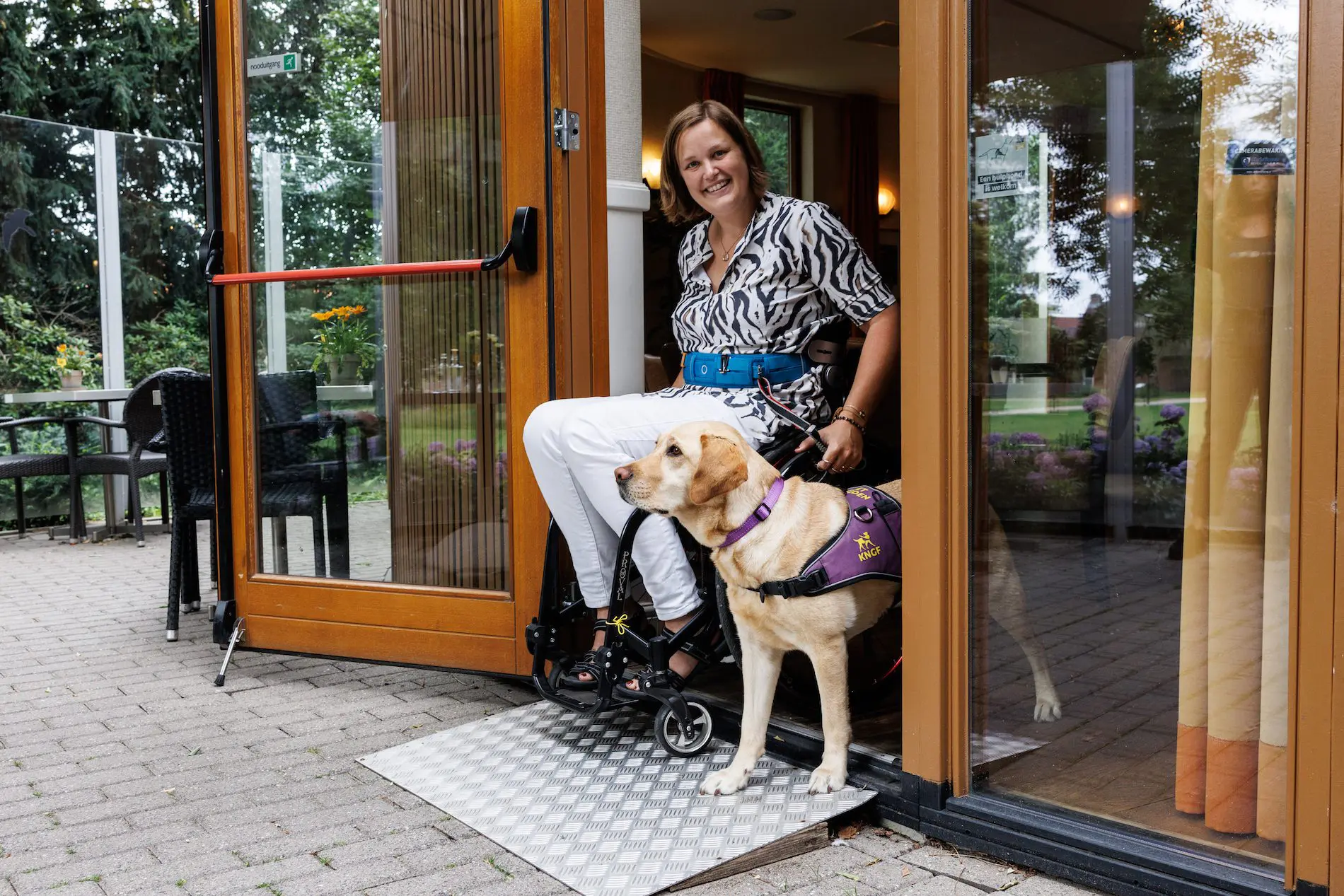 Mayke en assistentiehond Roos in de deuropening van een cafe/restaurant