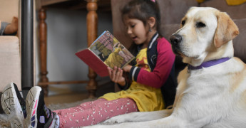 Kind zit naast hond een boekje te lezen