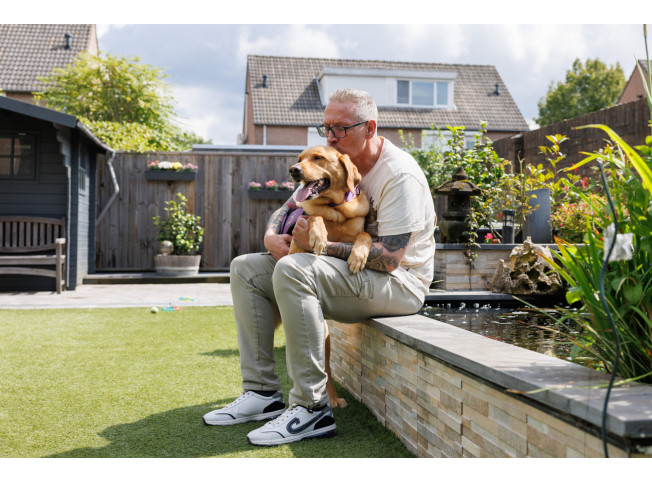 Alex zit in tuin op vijverrand met Hero op schoot