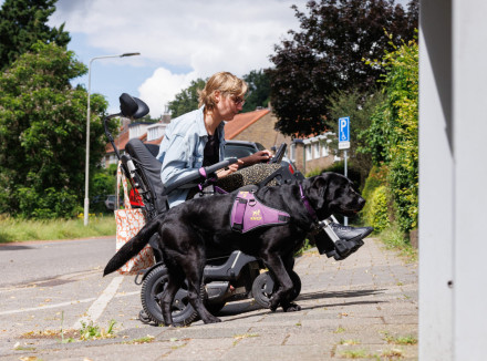 Nynke in een rolstoel met haar assistentiehond naast haar op de stoep