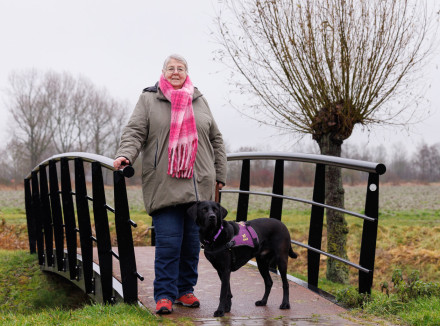 Klazien staat buiten op een bruggetje met haar PTSS-assistentiehond hero