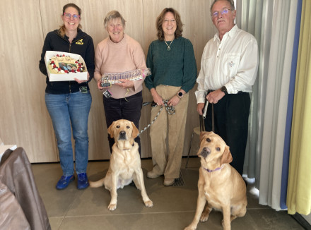 Groepsportret van familie Daaleman, KNGF directeur Monique en puppyinstructeur Maaike. Er zijn ook 2 honden op te zien en Maaike houdt een feestelijke taart vast.