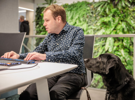 Vincent achter zijn bureau aan het werk met geleidehond Micha naast hem