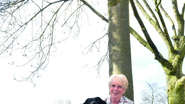 Een dame zit op haar hurken naast een zwarte labrador