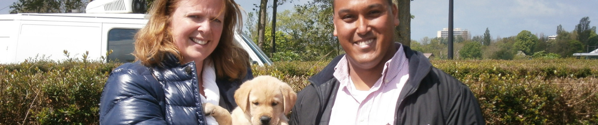 Familie Hooper, 2 volwassenen en 2 kleine kinderen, staat buiten met een blonde pup in hun armen
