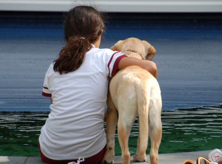 Hond en meisje op de rug. Hond staat naast het meisje die zit en haar arm over de hond heeft