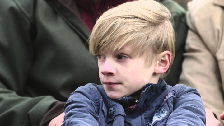 Jongetje uit video Autismegeleidehond kijkt opzij en is omringd door zijn ouders
