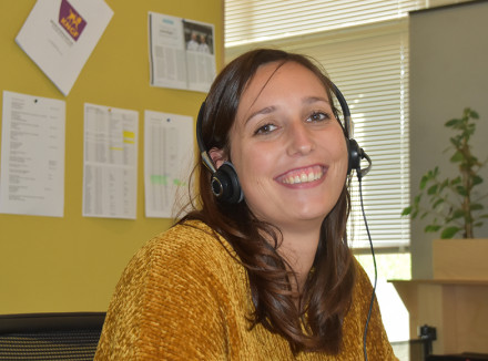 Eva met headset op aan het werk achter haar bureau