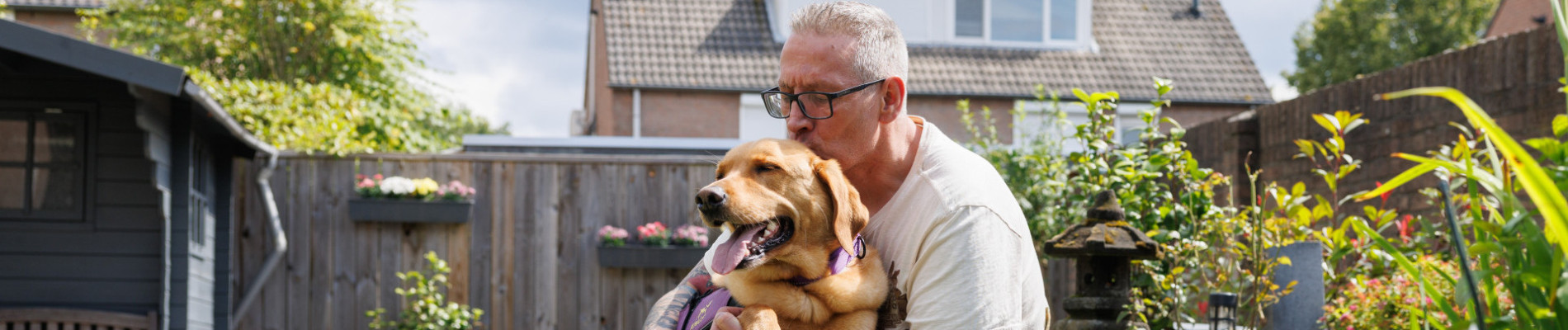 Alex zit op een rand van tuinvijver en knuffelt zijn hulphond op schoot.