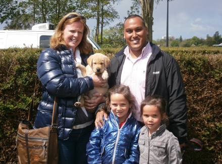 Familie Hooper, 2 volwassenen en 2 kleine kinderen, staat buiten met een blonde pup in hun armen
