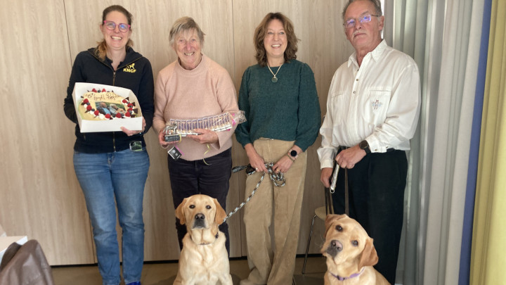 Groepsportret van familie Daaleman, KNGF directeur Monique en puppyinstructeur Maaike. Er zijn ook 2 honden op te zien en Maaike houdt een feestelijke taart vast.