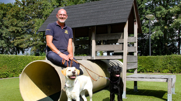 Medewerker Gert zit op een speeltoestel met een blonde en zwarte hond bij zijn voeten