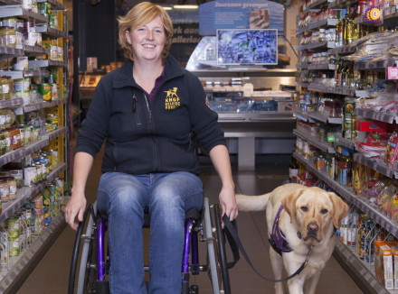 Marlouke zit in een rolstoel in de supermarkt met een assistentiehond naast haar