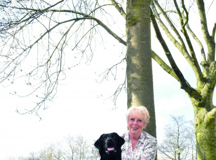 Een dame zit op haar hurken naast een zwarte labrador