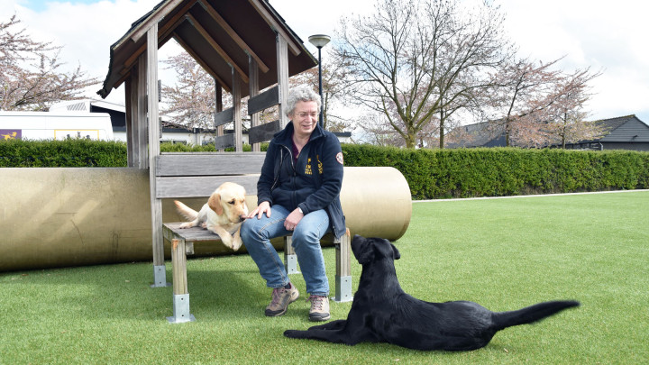 Carla zit bij een speeltoestel met twee geleidehonden in opleiding