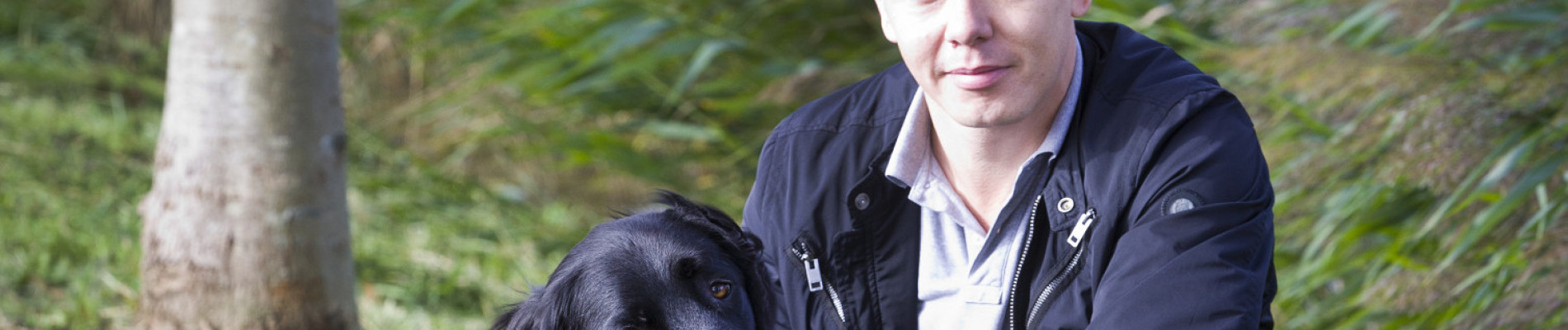 Justin zit met zwarte buddyhond Remi voor zich in het gras