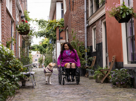 Claudia in rolstoel in pittoresk straatje met haar hulphond ernaast