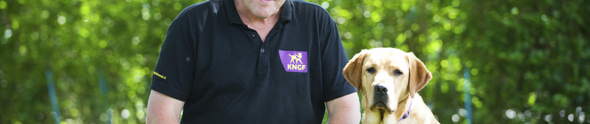 Kees zit naast een blonde labrador in het gras
