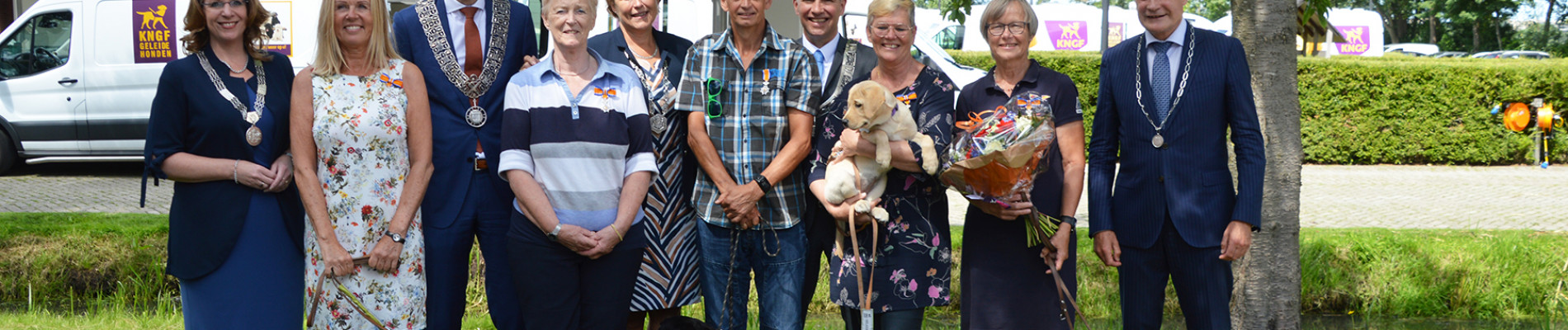 Vrijwilligers met burgemeesters in de tuin van KNGF geleidehonden met twee honden.