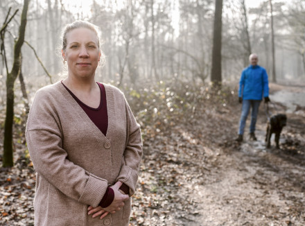 Portret van Maike in het bos. Op de achtergrond Stefan en zijn geleidehond Winston