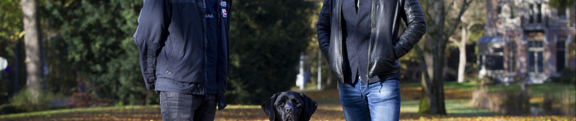 Portret van Maikel, blindengeleidehond Orris en Gerard Ekdom in een herfstig landschap