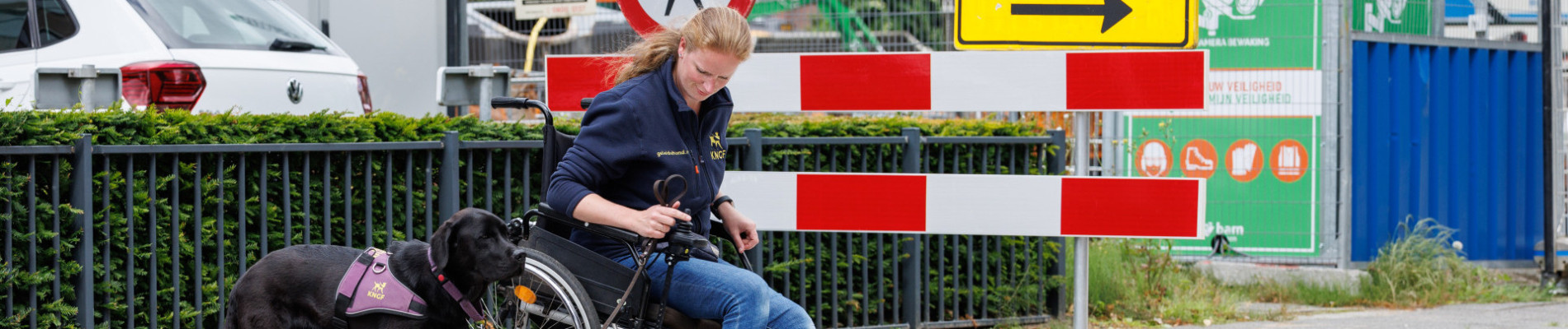 Tessa zit in een rolstoel en samen met de hond naast haar staan ze aan de rand van de stoep