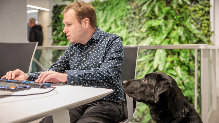 Vincent achter zijn bureau aan het werk met geleidehond Micha naast hem