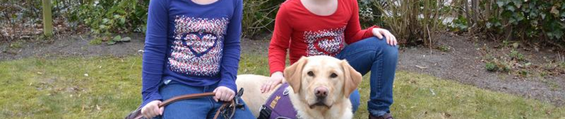 Kinderen zitten naast buddyhond Nando met paars KNGF-dekje op het gras in de tuin