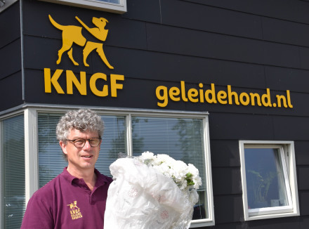 Herman staat voor het KNGF Geleidehonden gebouw met een bos prachtige witte anjers in zijn handen.