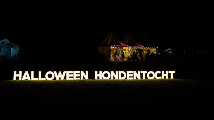 donker bos met verlichte letters halloween hondentocht en een verlicht kraampje op de achtergrond