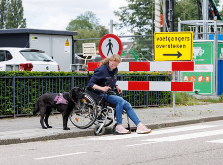 Tessa zit in een rolstoel en samen met de hond naast haar staan ze aan de rand van de stoep