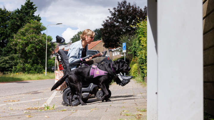 Nynke in een rolstoel met haar assistentiehond naast haar op de stoep