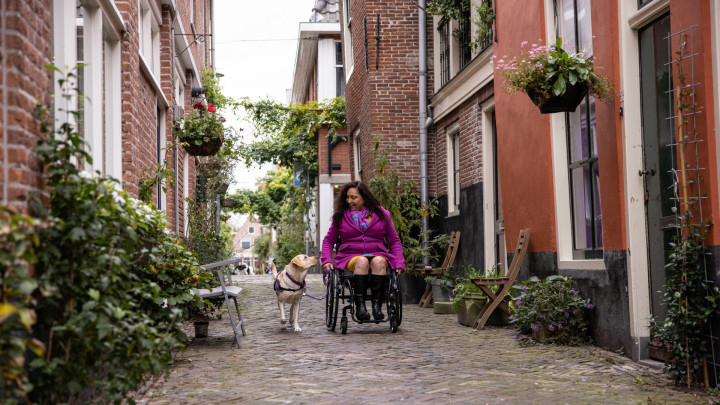 Claudia in rolstoel in pittoresk straatje met haar hulphond ernaast