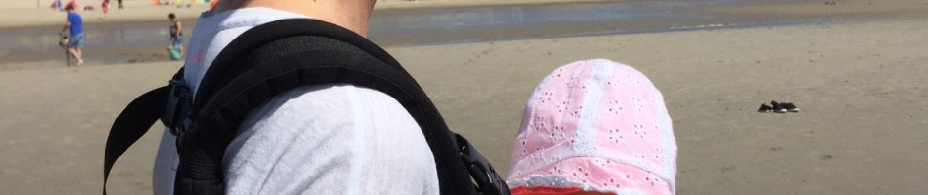 Anneloes kijkt uit op het strand met haar baby in een draagzak op haar buik