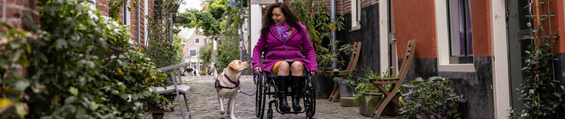 Claudia in rolstoel in pittoresk straatje met haar hulphond ernaast