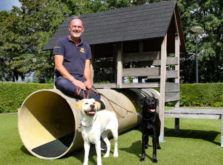 Medewerker Gert zit op een speeltoestel met een blonde en zwarte hond bij zijn voeten