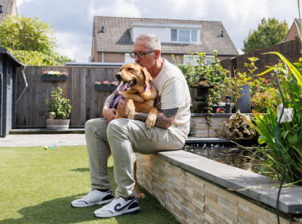 Alex zit op een rand van tuinvijver en knuffelt zijn hulphond op schoot.