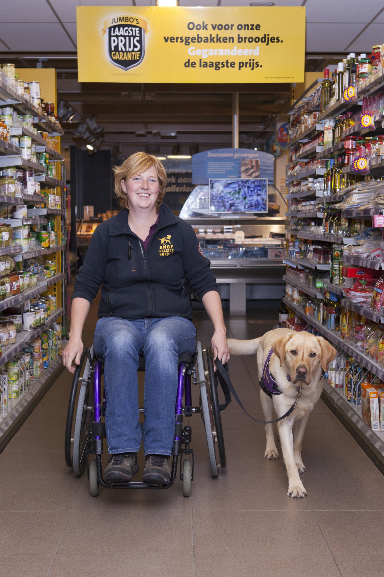 Marlouke in een rolstoel in supermarkt met assistentiehond ernaast