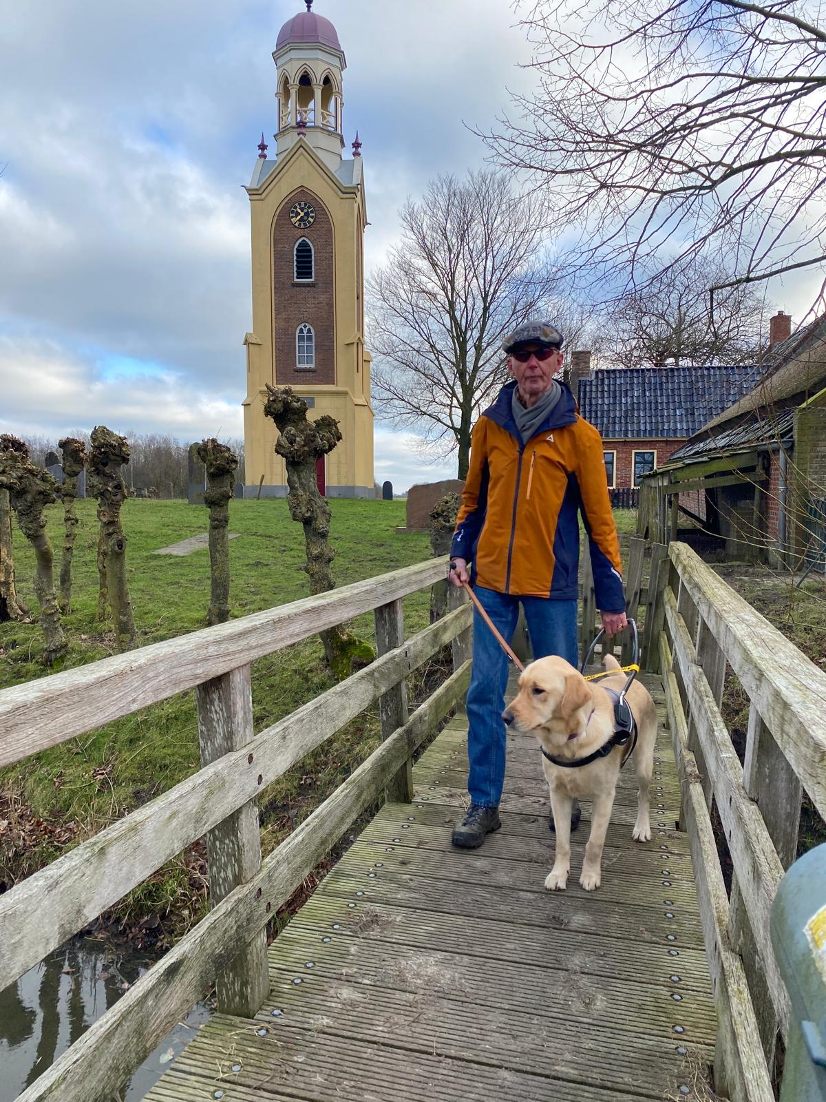 Albert en zijn geleidehond op een bruggetje bij de kerkklok