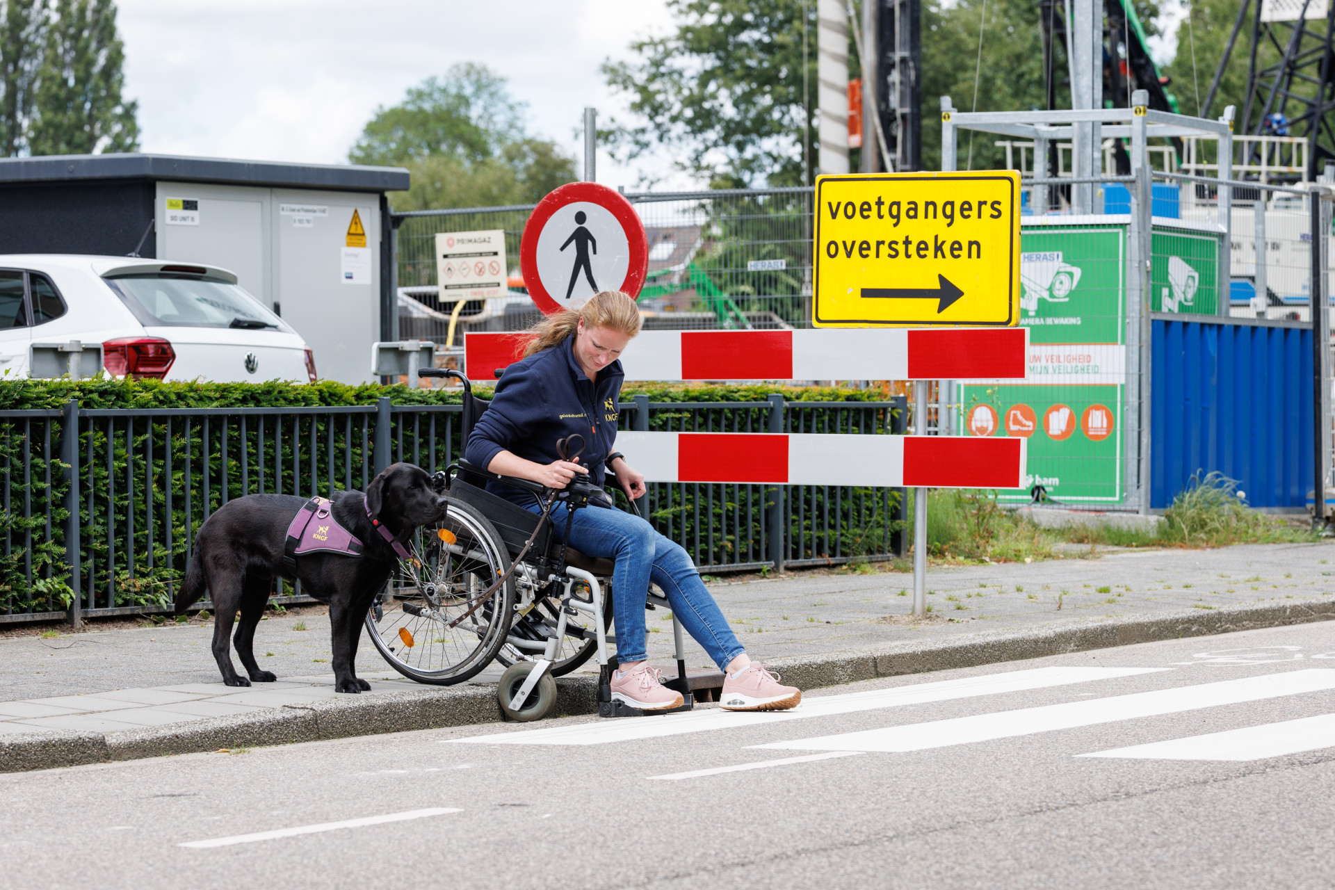 Tessa zit in een rolstoel en samen met de hond naast haar staan ze aan de rand van de stoep