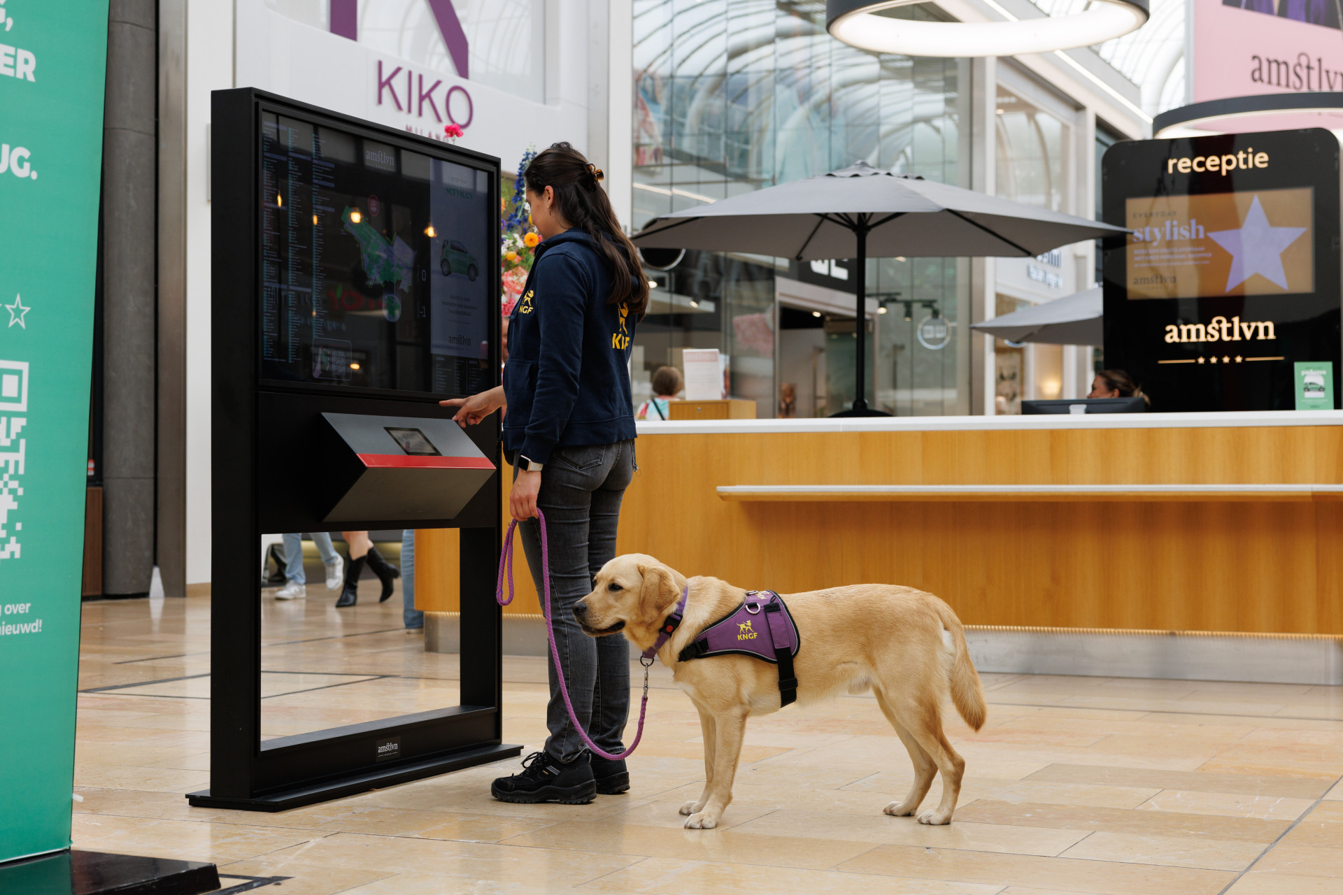 Saraya staat bij een bord en de blonde hond staat achter haar