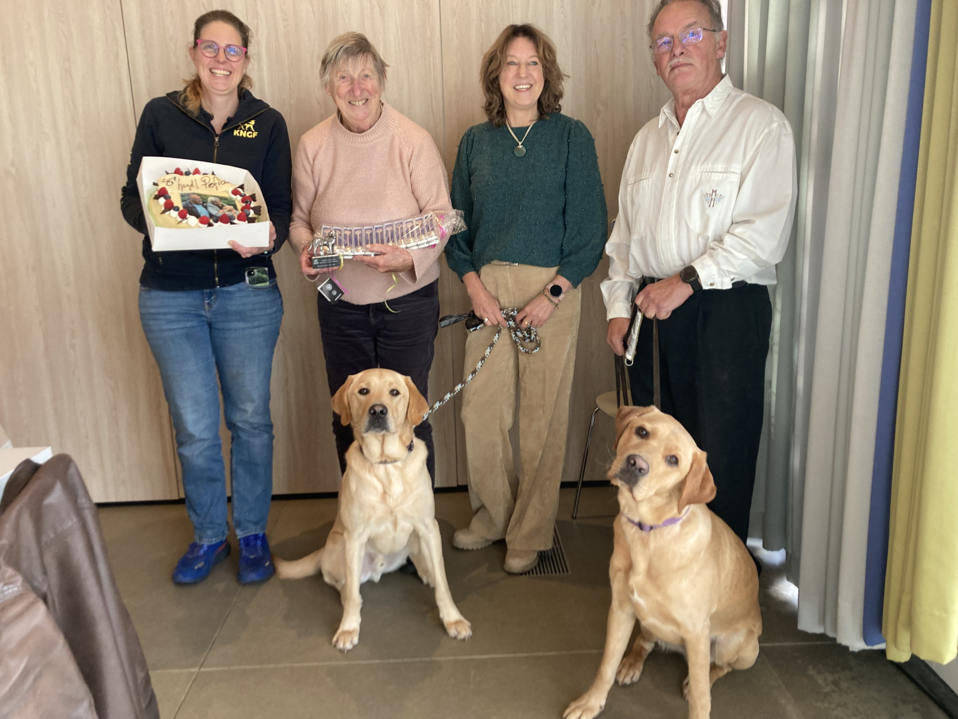 Groepsportret van familie Daaleman, KNGF directeur Monique en puppyinstructeur Maaike. Er zijn ook 2 honden op te zien en Maaike houdt een feestelijke taart vast.