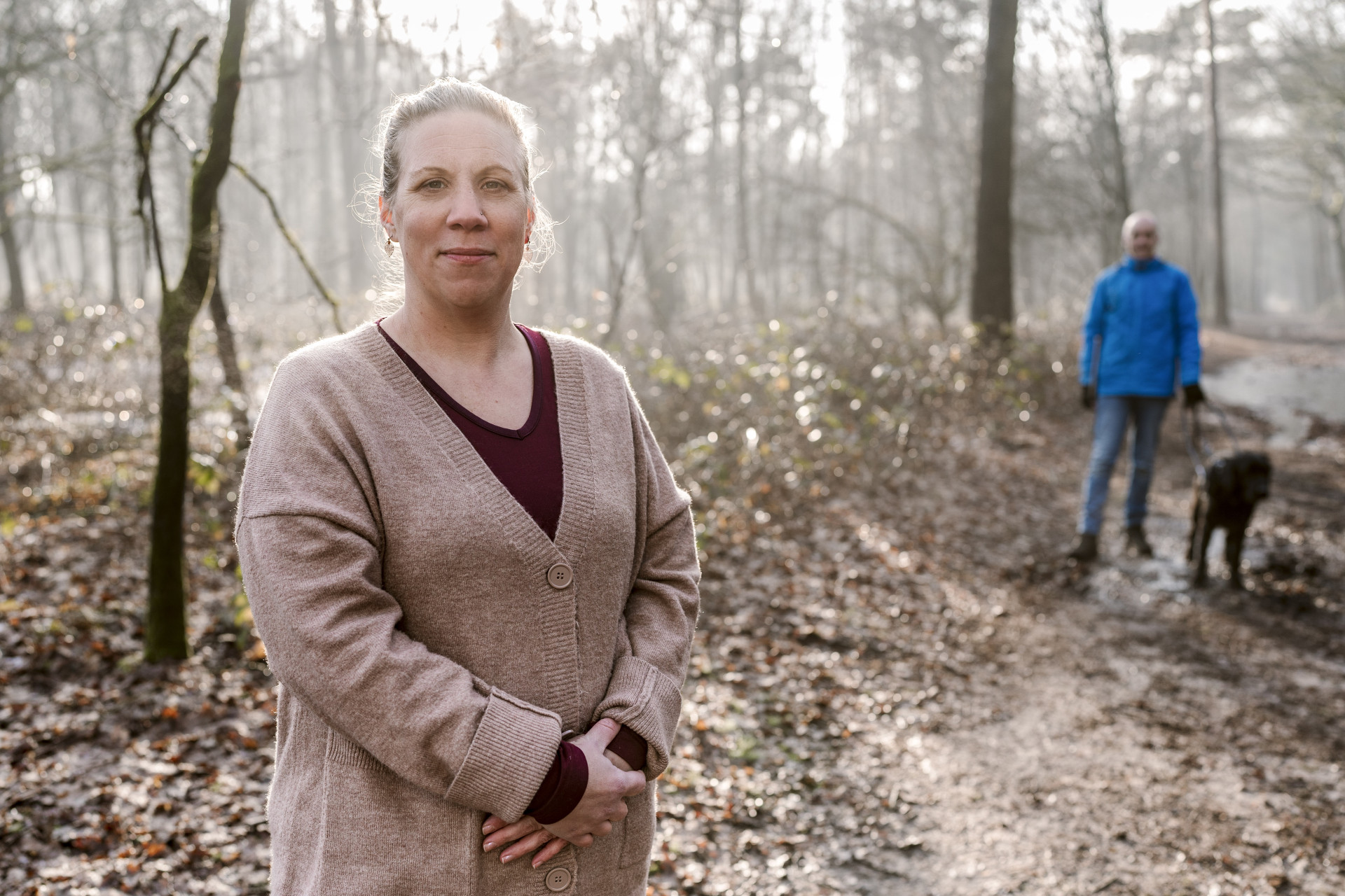 Portret van Maike in het bos. Op de achtergrond Stefan en zijn geleidehond Winston