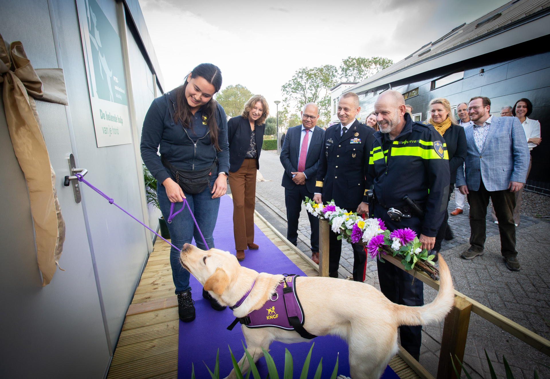 deur word opengetrokken door blonde hond, eromheen verschillende mensen in uniform