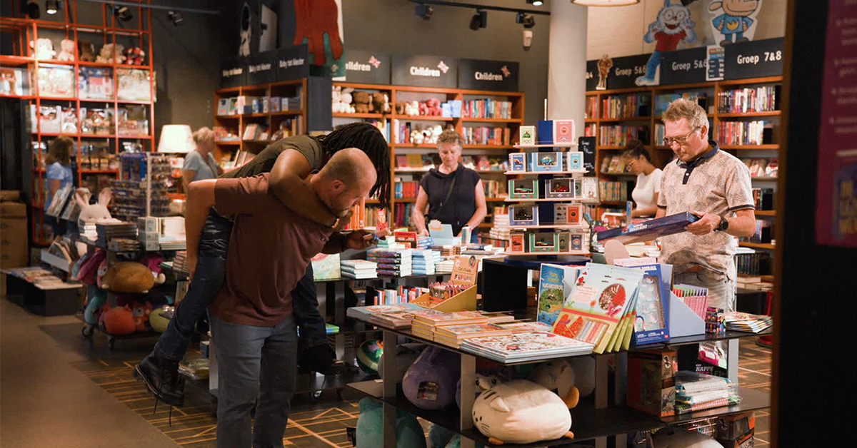 man loopt met man op rug door boekenwinkel