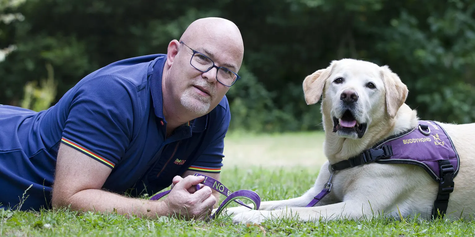 John samen met zijn Buddyhond liggend op het gras kijkend naar de camera